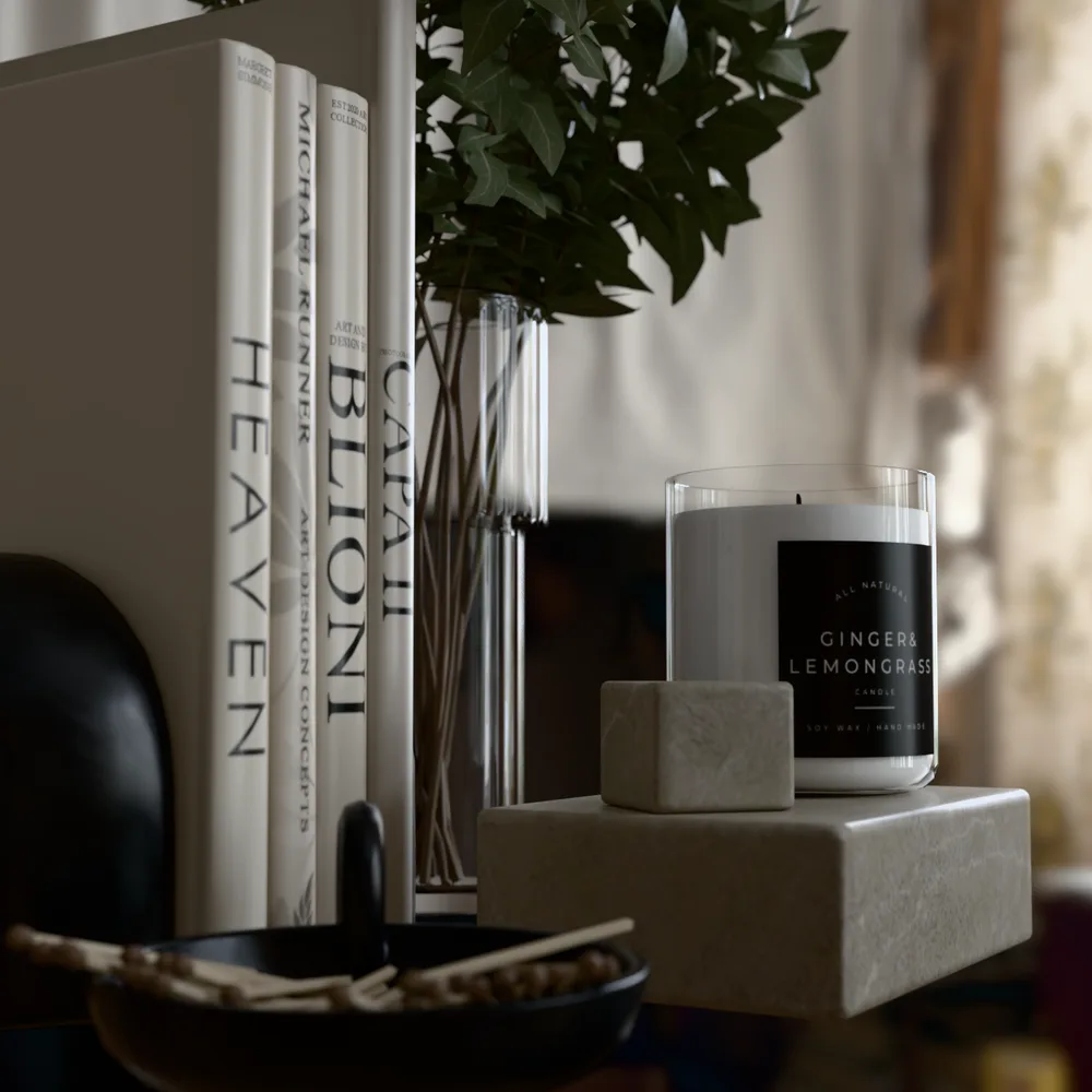 Soy candle on marble blocks beside coffee table books and a glass vase, path traced in the browser with soft window light